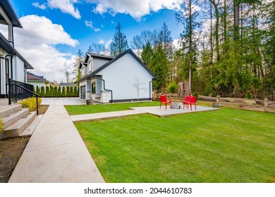 Backyard Of A Large Home With Green Grass And Four Red Chairs