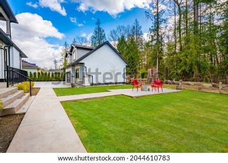backyard of a large home with green grass and four red chairs