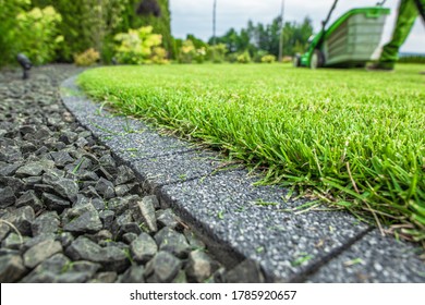 Backyard Lawn Grass Field Cobble Edge. Grass Mowing And Edges Finishing. Gardening And Landscaping Industry Theme.