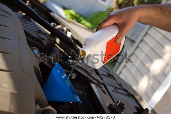 A backyard mechanic pours motor oil into\
the engine at the end of an oil change.  Home maintenance is\
becoming more popular during hard economic\
times.