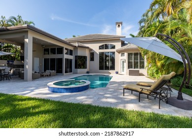 Backyard Of A Modern House With Swimming Pool, Artificial Grass, Trees, Chairs And An Umbrella.