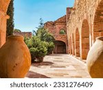 Backyard of an old hacienda with small trees and green plants, brick walls with pillars and arches, two huge clay vases as decoration, sunny day with a clear blue sky in Zacatecas Mexico