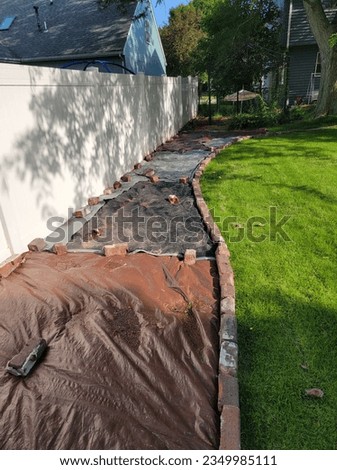 A backyard project in progress, using tarps to kill grass within a brick-lined section 