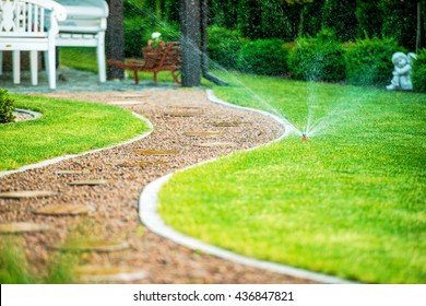 Backyard Residential Garden Grass Field Sprinklers In Action. Garden Path.