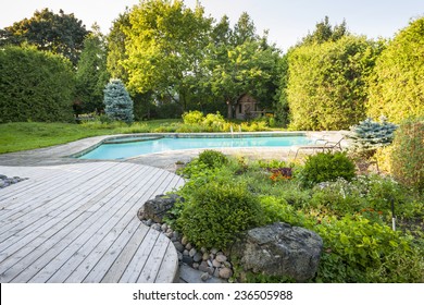 Backyard rock garden with outdoor inground residential swimming pool, curved wooden deck and stone patio