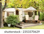 Backyard with RV house with garden furniture. Two deckchairs near outside caravan trailer. Cozy Campsite on caravan or camper van in forest. Trailer of mobile home stands in garden in camping. 