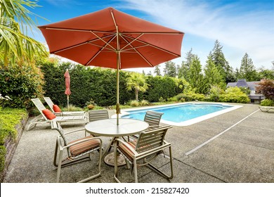 Backyard With Swimming Pool, Deck Chairs And Patio Table With Umbrella