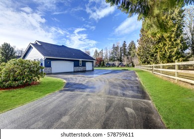 Backyard View Of Blue Rambler Home With Three Car Attached Garage And Driveway.  Northwest, USA