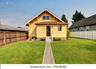 Backyard view of yellow siding craftsman house. White fence, green grass and concrete walkway. Northwest, USA