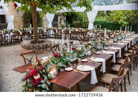 in backyard of villa in Tuscany there is a reception wooden table decorated with cotton and eucalyptus compositions, glasses, candles and plates are placed on table