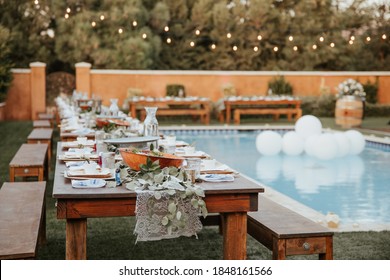 Backyard Wedding Setting - Wooden Tables With Bohemian Decor Around Swimming Pool.