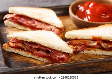 Bacon butty is a British sandwich consisting of crispy bacon, butter, and sauce closeup in the wooden tray on the table. Horizontal