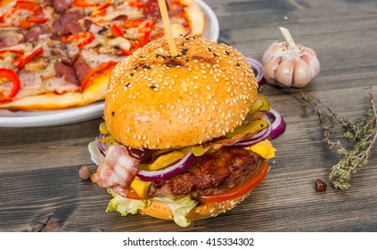 Bacon Cheese Burger With Beef Patty Tomato Onion And Pizza On A Wooden Table