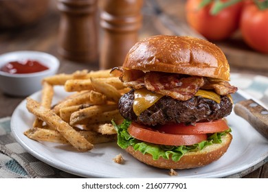 Bacon cheeseburger with lettuce and tomato  on a toasted bun and french fries on a plate - Powered by Shutterstock