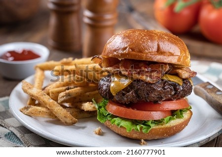 Bacon cheeseburger with lettuce and tomato  on a toasted bun and french fries on a plate