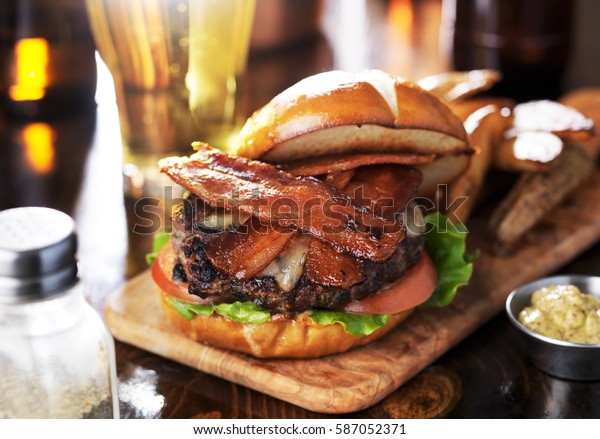 bacon cheeseburger on toasted\
pretzel bun served with fries and beer shot with selective\
focus