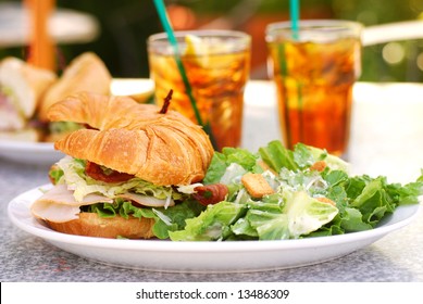 Bacon, Lettuce, Tomato, Turkey And Avocado Sandwich On A Croissant At An Outdoor Cafe