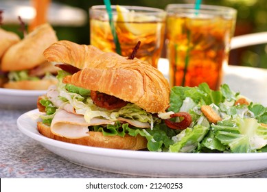 Bacon, Lettuce, Tomato, Turkey And Avocado Sandwich On A Croissant At An Outdoor Cafe