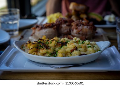 A Bacon Macaroni And Cheese Dish Plated In A Boat Shaped Platter, And Garnished With Chopped Green Scallions.