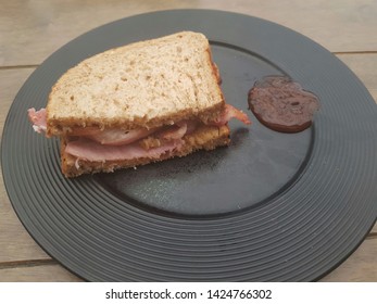 Bacon Sandwich On Granary Bread. A Black Plate With Brown Sauce. Room For Text.