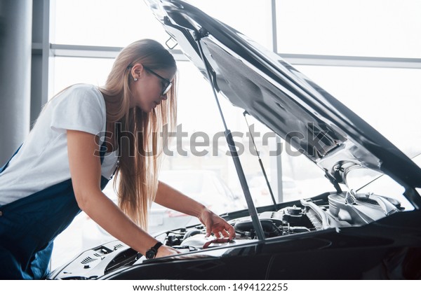 Bad battery must be\
replaced. On the lovely job. Car addicted woman repairs black\
automobile indoors.