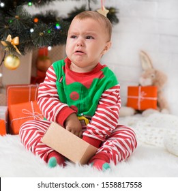 Bad Christmas. Little Baby Elf With Present Box Crying Near Xmas Tree, Waiting For Gifts