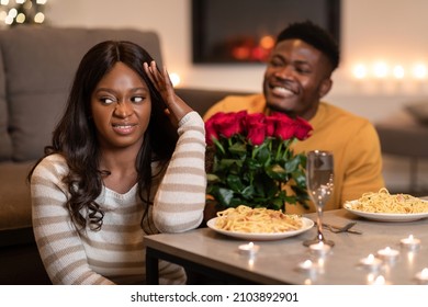 Bad Date. Discontented Black Woman Covering Face Expressing Disgust While Boyfriend Giving To Her Flowers Congratulating On Valentine's Day At Home. Selective Focus