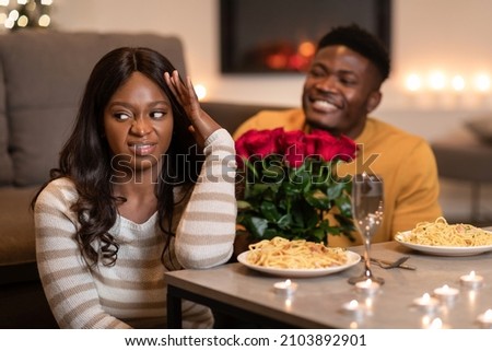 Bad Date. Discontented Black Woman Covering Face Expressing Disgust While Boyfriend Giving To Her Flowers Congratulating On Valentine's Day At Home. Selective Focus