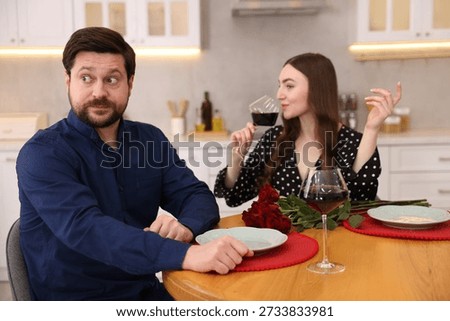 Bad date. Embarrassed man ignoring woman with wine at table during dinner indoors