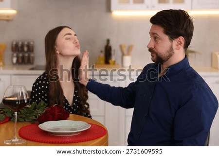 Bad date. Embarrassed man refusing kiss from woman at table during dinner indoors