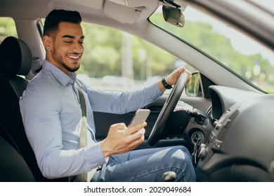Bad driving habits, unsafe driving, driving and gadgets concept. Cheerful arab man entrepreneur going to office by auto, using cellphone while driving car, chatting with someone, side view, copy space