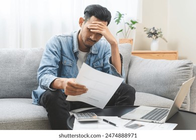 Bad financial concept, frustrated asian young man, male having debt, reading paper report from bank, stress by calculate expense from invoice or bill not able money to pay mortgage or loan, bankruptcy