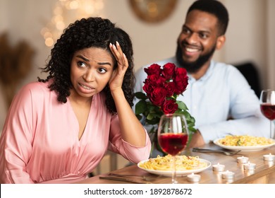 Bad First Impression And Blind Date Concept. Dissatisfied shocked black woman rejecting excited emotional obsessed man who giving her flowers, young couple sitting at table in cafe