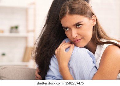 Bad Friend. Girl Rolling Eyes Embracing Crying Roommate Pretending To Be Good Sitting On Sofa At Home. Selective Focus