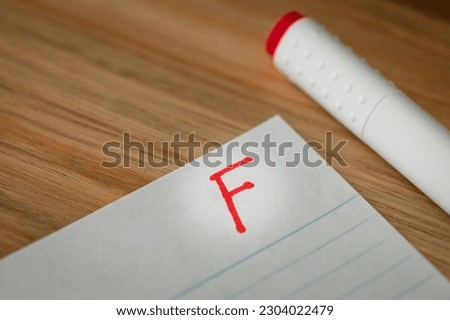 Bad grade of F is written with red pen on the test. Disqualification and flunked concept.