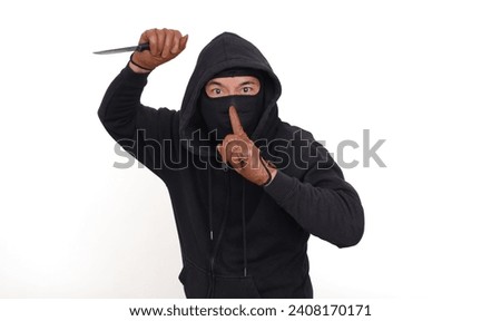 Bad guy in black hoodie, raising his right hand with a knife and gesturing not to make any noise