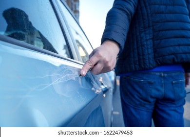 Bad guy scratching the car door with a screwdriver in the parking lot on the street. Damage of property from revenge for treason or betrayal, or threat. Auto insurance fraud or vandalism.