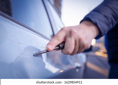 Bad guy scratching the car door with a screwdriver in the parking lot on the street. Damage of property from revenge for treason or betrayal, or threat. Auto insurance fraud or vandalism. 