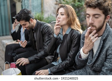 Bad habits - group of young friends smoking cigarettes together outdoors. Unhealthy addiction concept.