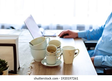 Bad lifestyle Caffeine addicted concept. Many cups of coffee on the desk. A man working from home on laptop as the background. Drinks too much coffee caffeine addiction anxious and crazy in maniac. 
