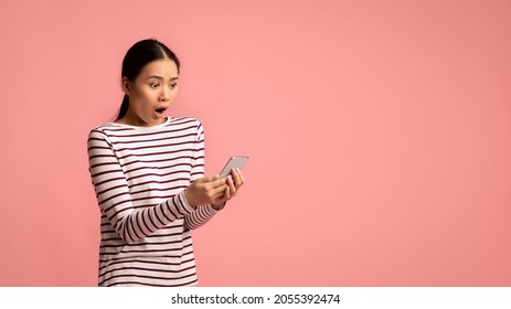 Bad Message. Young Asian Woman Looking At Smartphone With Shock, Reading Unpleasant Sms, Portrait Of Emotional Korean Female With Cellphone In Hands Standing Over Pink Studio Background, Free Space
