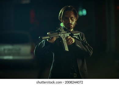 Bad Movie Hero Aiming  An Automatic Gun In His Hands In An Industrial Zone At Night. 