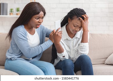 Bad news. Despaired Black Woman Showing Smartphone With Unpleasant Message To Her Friend, Sitting On Sofa At Home.