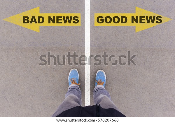 Bad news and good news text on yellow arrows on\
asphalt ground, feet and shoes on floor, personal perspective\
footsie concept