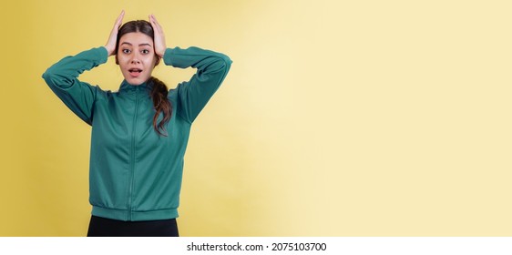 Bad News. Looks Shocked. Young Emotional Girl In Green Track Suit Isolated On Yellow Studio Background In Neon. Concept Of Emotions, Trend, Style, Facial Expression, Youth, Aspiration. New Fashions