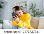 Bad news on device screen. Upset asian woman frustrated by problem with work or relationships, sitting on couch, feeling despair and anxiety, loneliness, having psychological trouble