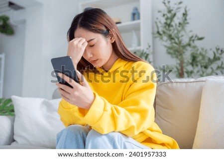 Bad news on device screen. Upset asian woman frustrated by problem with work or relationships, sitting on couch, feeling despair and anxiety, loneliness, having psychological trouble