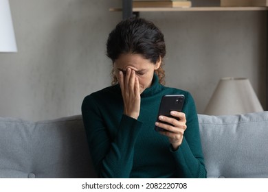Bad news on screen. Confused frustrated young latin lady cover face with palm turn away from cell seeing important call missed. Desperate millennial woman get message on phone about dismissal from job - Shutterstock ID 2082220708