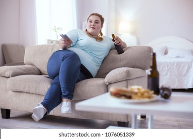 Bad Nutrition. Stout Red-head Woman Drinking Beer While Watching Television