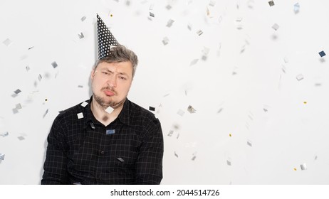 Bad Party. Lonely Birthday. Ruined Celebration. Introvert Personality. Disappointed Sad Man In Festive Hat With Confetti Fall Isolated On Copy Space White Banner Background.